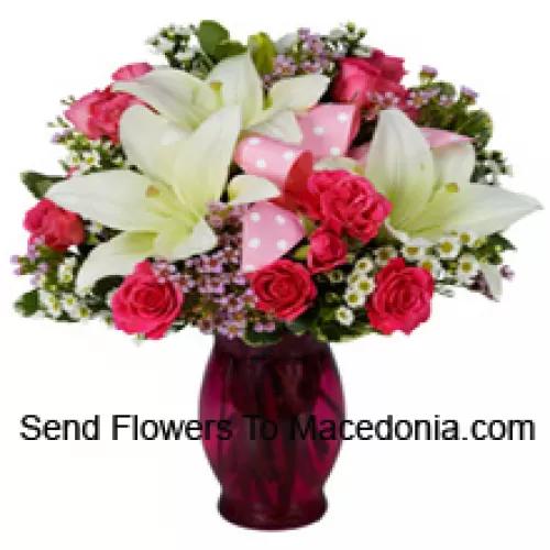 Roses roses et lys blancs avec des remplissages saisonniers dans un vase en verre